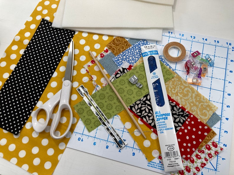 May include: A close-up of a sewing project with various fabrics, tools, and supplies. The fabrics are a mix of patterns, including polka dots, floral, and geometric designs. The tools include scissors, a ruler, a seam ripper, and a zipper. The supplies include a piece of batting, a roll of tape, and a set of fabric clips.