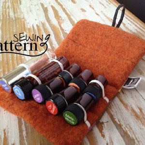 Puede incluir: Una bolsa de fieltro marrón con una correa negra, que contiene siete pequeños frascos de vidrio con tapones de goma y etiquetas. Las etiquetas tienen texto como "Lavender", "Oregano" y "Melaleuca". La bolsa está sobre una superficie de madera blanca. "Sewing pattern" está escrito en negro en la bolsa.