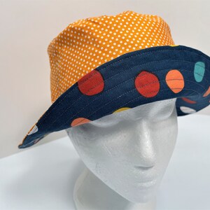 May include: A reversible bucket hat with a navy blue and white polka dot pattern on one side and a navy blue side with colorful polka dots on the other side.