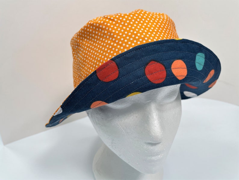 May include: A reversible bucket hat with a navy blue and white polka dot pattern on one side and a navy blue side with colorful polka dots on the other side.