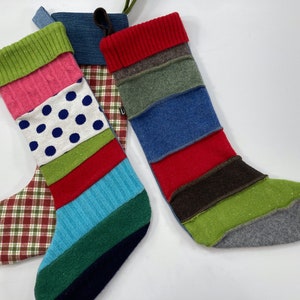 Pode incluir: Três meias de Natal coloridas feitas com tecido reutilizado. As meias são listradas com várias cores, incluindo vermelho, verde, azul, rosa, branco e marrom.