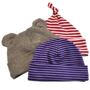 May include: Three knitted baby hats in different colors and styles. One hat is gray with bear ears, one is red and white striped, and one is purple and white striped.