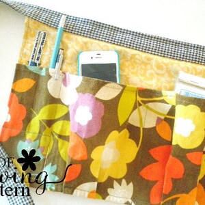 May include: A brown fabric apron with multiple pockets, featuring a floral print in shades of yellow, orange, and purple. The apron has a black and white checkered trim and includes a cell phone pocket, a pencil holder, and a pocket for a small notepad.