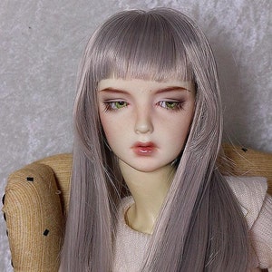 May include: A doll with long, straight, silver-grey hair, wearing a light pink sweater. The doll has a light complexion and green eyes.