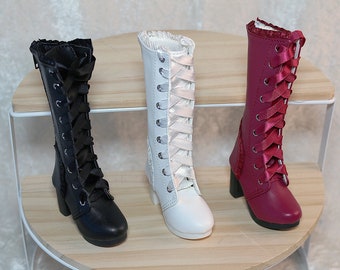 May include: Three miniature lace-up boots in black, white, and burgundy. Each boot features a high heel and is laced with satin ribbon. The boots are displayed on a two-tiered wooden shelf with a white metal frame.