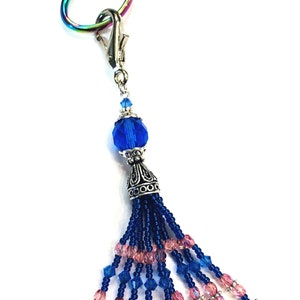 May include: Rainbow unicorn-shaped scissors with a blue and pink beaded tassel. The tassel has a silver charm and a blue and white floral bead at the bottom.