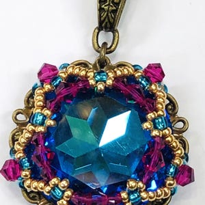 May include: A teal blue crystal pendant with gold and pink beads, set in an ornate bronze frame.
