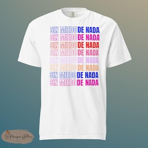 May include: White t-shirt featuring the phrase "SIN MIEDO DE NADA" in a repeating pattern of blue, red, pink, and orange. The shirt is a casual style, suitable for everyday wear.