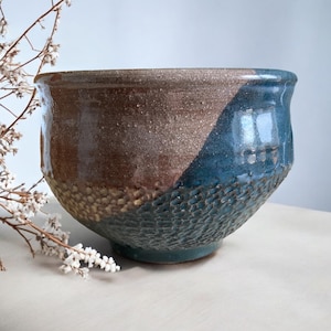 May include: A large, ceramic bowl with a textured, blue and brown glaze. The bowl has a wide, rounded base and a slightly flared rim.
