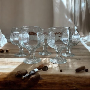 May include: Set of six clear glass stemmed goblets with a textured surface. The goblets are arranged on a wooden surface.