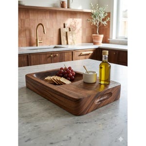 May include: A rectangular wooden serving tray with a recessed area for food. The tray holds crackers, red grapes, a small bowl with a spoon, and a bottle of olive oil. The tray has a handle on the side.