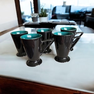 May include: Set of six black and teal ceramic mugs with a unique angled design. The mugs have a teal interior and a black exterior.