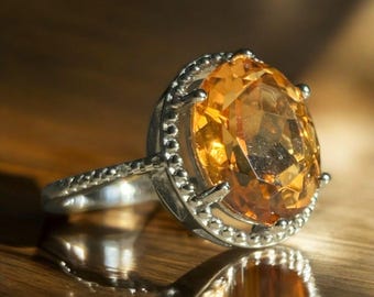 May include: A silver ring with a large, round, orange gemstone set in a beaded bezel.