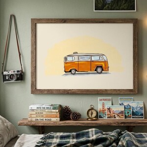 May include: A framed print of an orange and white vintage camper van against a yellow backdrop. A black camera hangs on the wall. A wooden shelf holds books, postcards, a compass, and pinecones. String lights are on the wall.