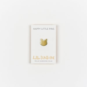 May include: A gold-colored cat face pin on a white card. The card reads "HAPPY LITTLE PINS" at the top and "hello SUNSHINE" with a website address at the bottom. The pin is centered on the card.