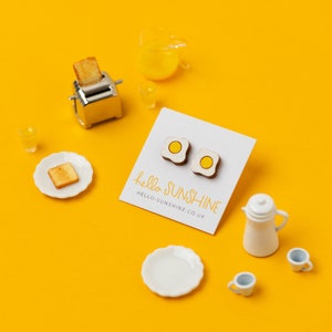 May include: A pair of wooden earrings shaped like fried eggs with yellow yolks. The earrings are on a white card with the text "hello sunshine" and "hello-sunshine.co.uk".