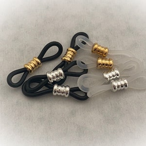 May include: A set of six eyeglass strap holders. Three are black with gold accents and three are clear with silver accents.