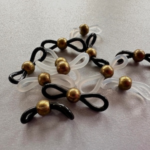 May include: A group of ten black and white eyeglass holders with gold-colored metal beads. The holders are made of a flexible material and are designed to hold eyeglasses securely.