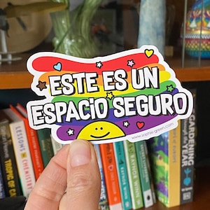 May include: A rainbow-colored sticker with the text "ESTE ES UN ESPACIO SEGURO" in white lettering. The sticker also features a yellow smiley face and stars. The website address "www.sophie-green.com" is printed at the bottom of the sticker.
