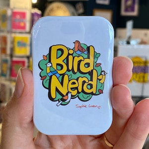 May include: White square tin with a colourful cartoon illustration of birds and the text "Bird Nerd" with the signature "Sophie Green" in red.