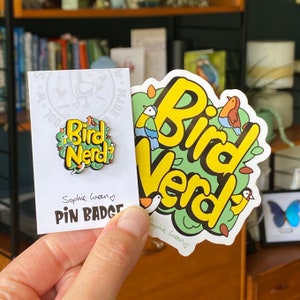 May include: A yellow and green sticker with the text "Bird Nerd" in a cartoon font. The sticker features a variety of colourful birds and leaves. The sticker is on a white background and has the text "Sophie Green" at the bottom.