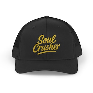 Puede incluir: Gorra de camionero negra con visera curva y parte trasera de malla. La gorra presenta el texto bordado "Soul Crusher" en oro, con una fuente cursiva. Un accesorio clásico.
