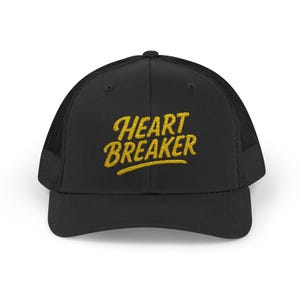 Gorra de camionero Heartbreaker. Gorra de béisbol atrevida con letras retro y diseño de corazón roto para quienes rompen las reglas con confianza. Letras amarillas.