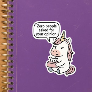 Peut inclure: Un carnet violet avec un autocollant représentant une licorne tenant une boîte de mouchoirs. L'autocollant dit "Zero people asked for your opinion."