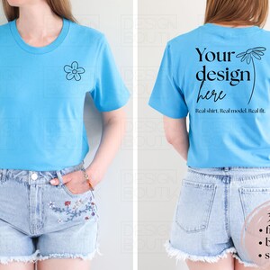 May include: A light blue t-shirt with a small black flower graphic on the front. The back of the shirt features the text "Your design here" with a floral design. The shirt is paired with denim shorts.