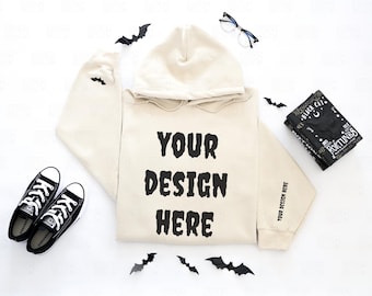 May include: A cream-colored hoodie with the text "YOUR DESIGN HERE" in black, paired with black sneakers, eyeglasses, and a book. Black bat cutouts are scattered around the hoodie. The hoodie has the text "YOUR DESIGN HERE" on the sleeve.