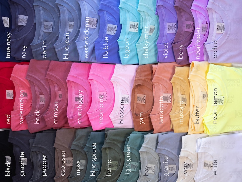 May include: A collection of folded t-shirts in various colors, including red, blue, and yellow. Each shirt is labeled with its color name, such as "true navy," "neon pink," and "neon lemon." The shirts are neatly arranged, showcasing a wide range of hues.