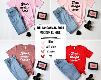 May include: Four Bella + Canvas 3001 t-shirts in different colors: lilac, soft pink, mauve, and red. Each shirt has the text "Your design here" printed on the front. The shirts are laid flat on a white surface with a pair of blue jeans, a small black heart, and a small black ampersand.