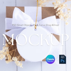 May include: A white, round ornament mockup with a gold string, resting on a brown gift box tied with a white ribbon. The word "MOCKUP" is displayed in white. Dried flowers and design software icons are also visible.