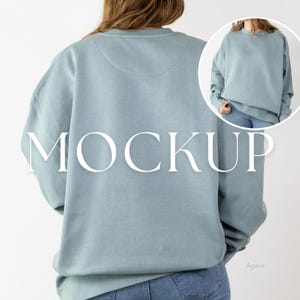 May include: A light blue sweatshirt with the word "MOCKUP" in large white letters. The sweatshirt is a crew neck style and is being worn by a person. The image also includes a smaller inset image of the sweatshirt.
