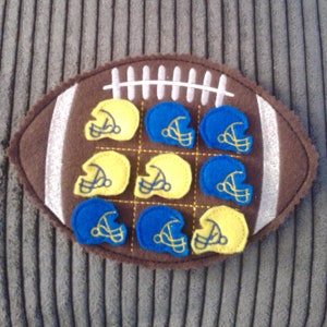 May include: A brown felt football with a white stitching design. The football has nine felt circles attached to it, alternating between blue and yellow. Each circle has a white outline and a white football helmet design inside.