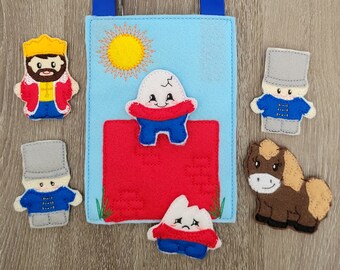 May include: A felt finger puppet set with a blue background and a red brick wall. The set includes a king, a soldier, a horse, and two characters with cracked eggshells for heads. The set is designed for storytelling and imaginative play.