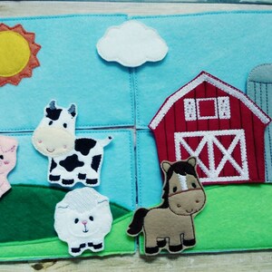 May include: A felt farm play set with a red barn, a silo, a yellow sun, a white cloud, a pink pig, a brown horse, a white sheep, and a black and white cow.