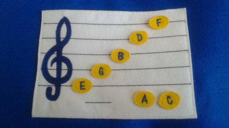 May include: A white felt music learning tool with a treble clef and yellow felt circles with the letters A, B, C, D, E, F, and G.
