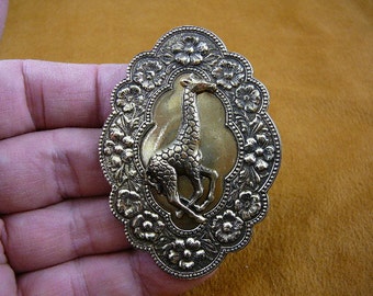 May include: A gold-toned metal brooch featuring a detailed floral design surrounding a raised image of a giraffe.