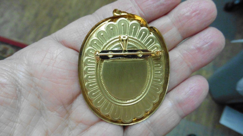 May include: Gold-toned oval brooch with a decorative border and a pin on the back.