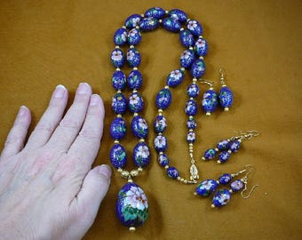 Puede incluir: Un conjunto de collar y pendientes de cloisonné azul y blanco con diseños florales. El collar tiene un gran colgante con un diseño floral.