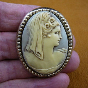 May include: Oval cameo brooch with a white cameo of a woman with a veil and a beaded gold-tone frame.