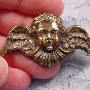May include: A gold-toned metal angel pin with wings and a cherub face. The angel is wearing a ruffled collar.