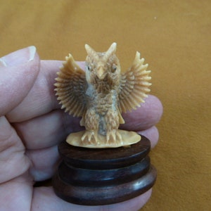 May include: A small, intricately carved owl figurine with outstretched wings, made of bone-like material and mounted on a dark wood base.