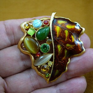 May include: A gold-tone leaf-shaped brooch with a brown enamel finish and a variety of colorful stones, including green, red, blue, and yellow.