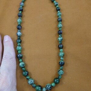 May include: A green and black gemstone necklace with a silver clasp. The necklace is made of round beads and is approximately 18 inches long.