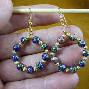May include: A pair of gold hoop earrings with blue, green, and pink enamel beads. The beads are round and have a floral design.