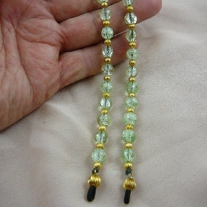 May include: A pair of green glass bead eyeglass chains with gold accents and black rubber tips.