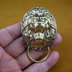 Puede incluir: Un llamador de puerta de cabeza de león dorado con un asa de anillo. La boca del león está abierta y su melena está detallada.