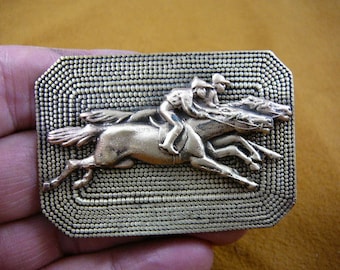 May include: A rectangular brass-toned belt buckle featuring a raised relief design of two jockeys riding galloping horses. The background of the buckle has a textured pattern of small, uniform dots, and the edges are beveled with a smooth finish.